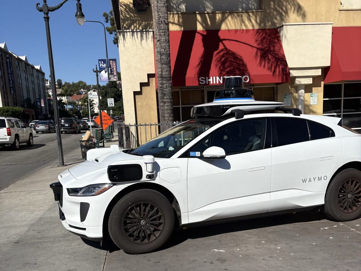 ロサンゼルスの街角に停まるWaymoのロボタクシー。白い車体の屋根の上に大きなセンサーがあり、車体の前方にもカメラやセンサーが付いている